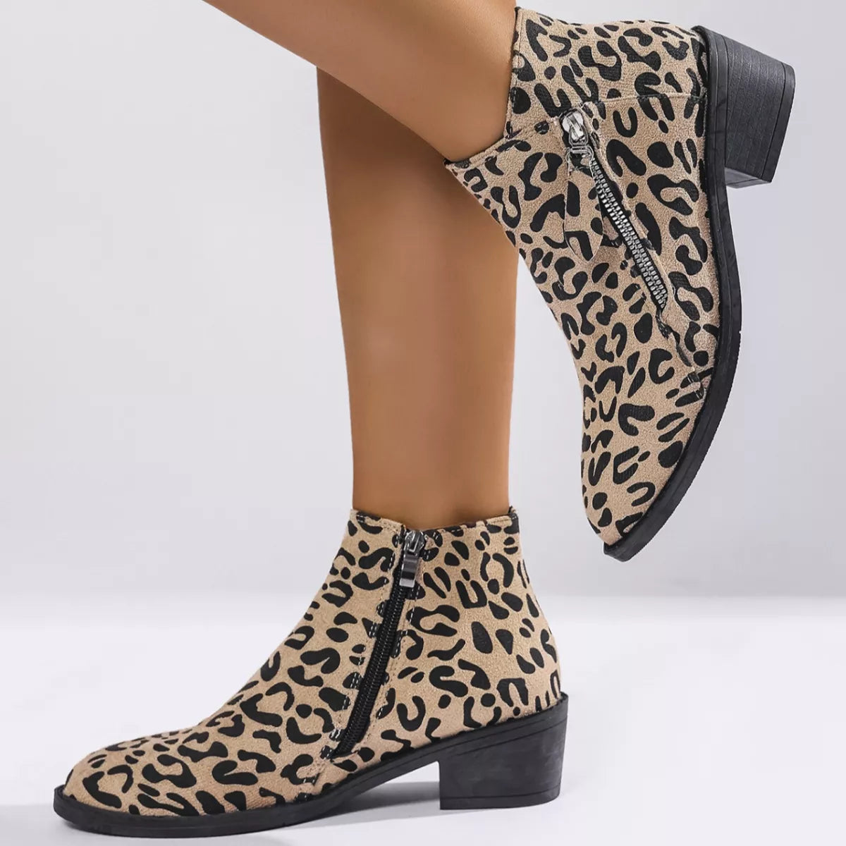 Woman wearing khaki leopard-print ankle boots with block heels and side zipper details.