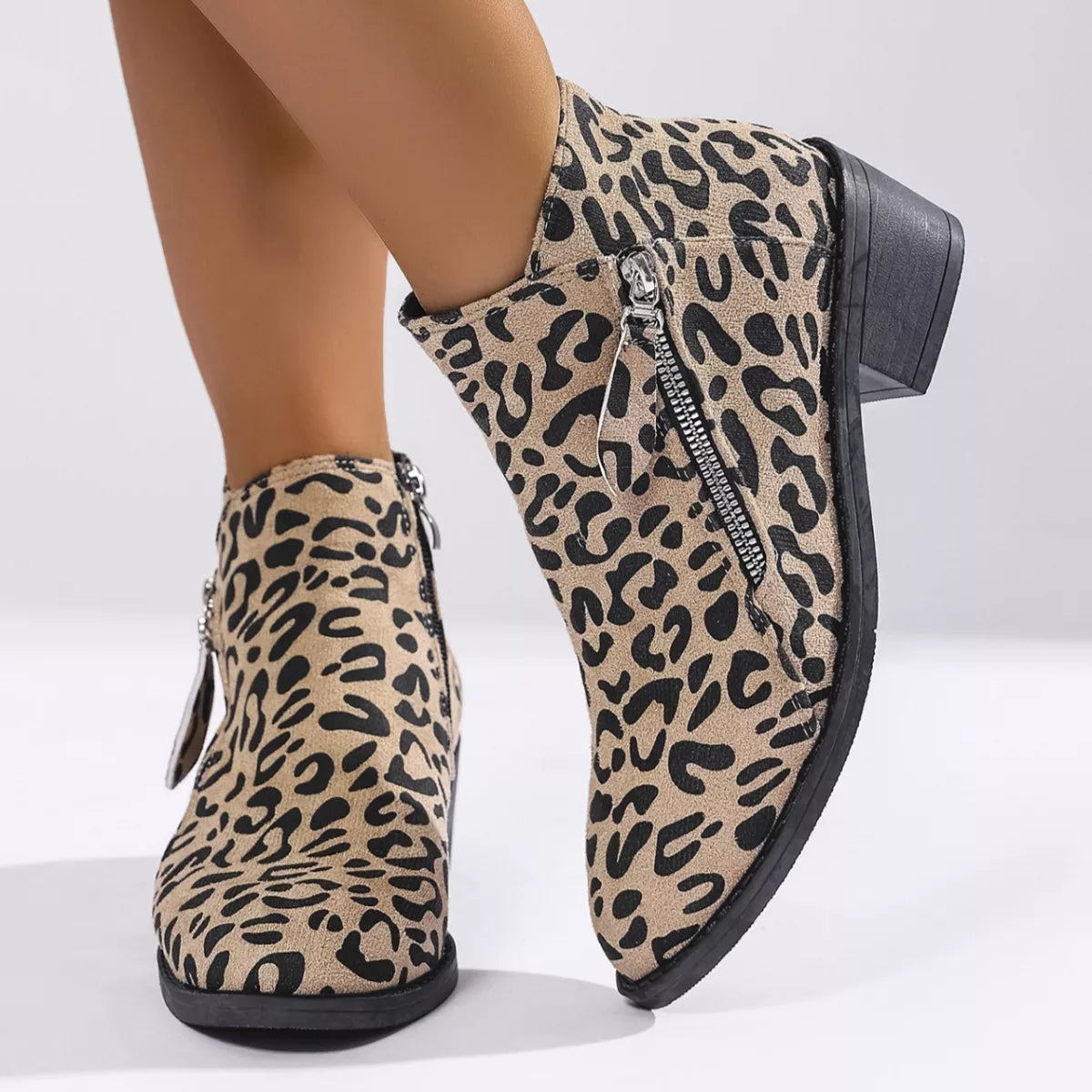 Woman wearing khaki leopard-print ankle boots with block heels and side zipper details.