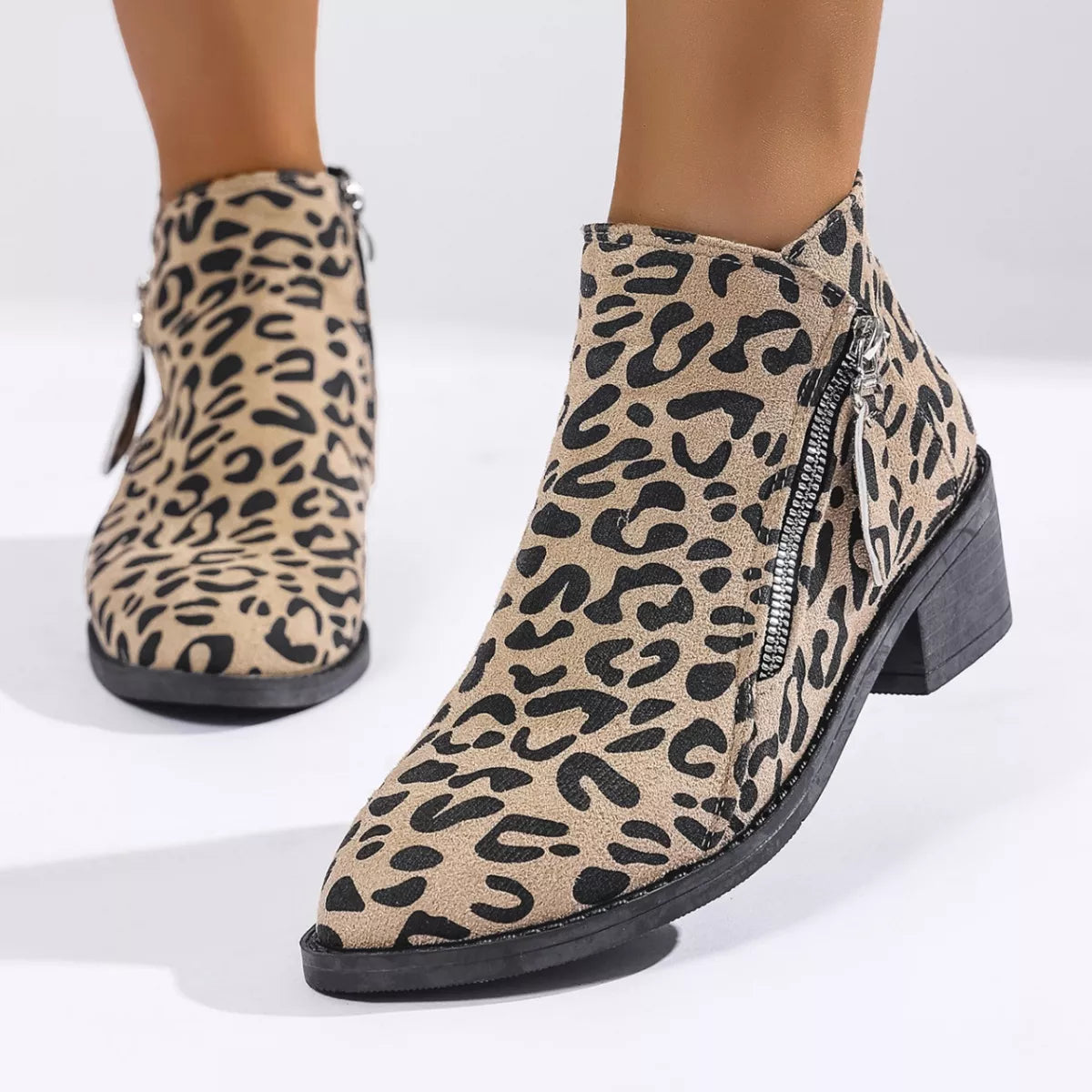 Woman wearing khaki leopard-print ankle boots with block heels and side zipper details.