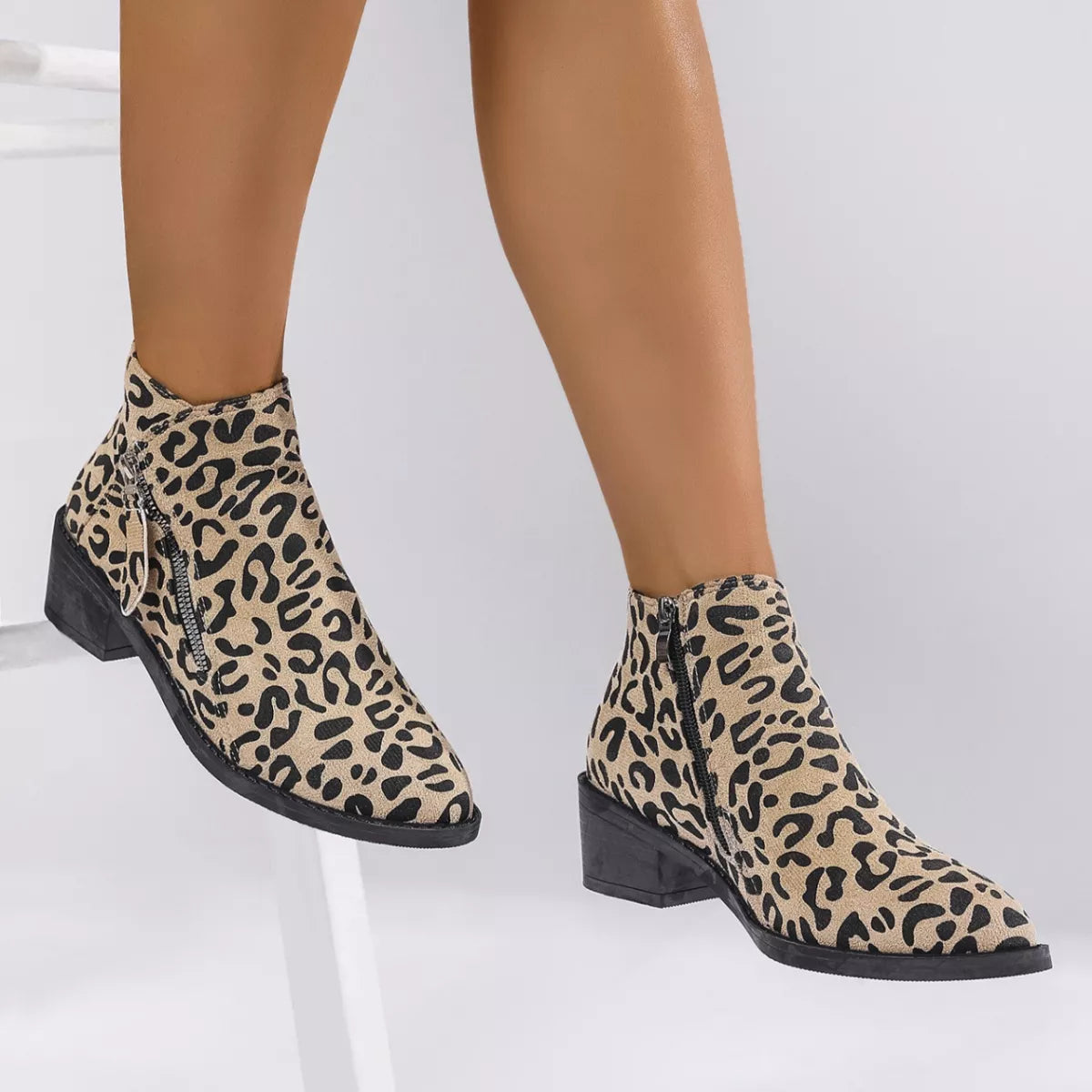 Woman wearing khaki leopard-print ankle boots with block heels and side zipper details.
