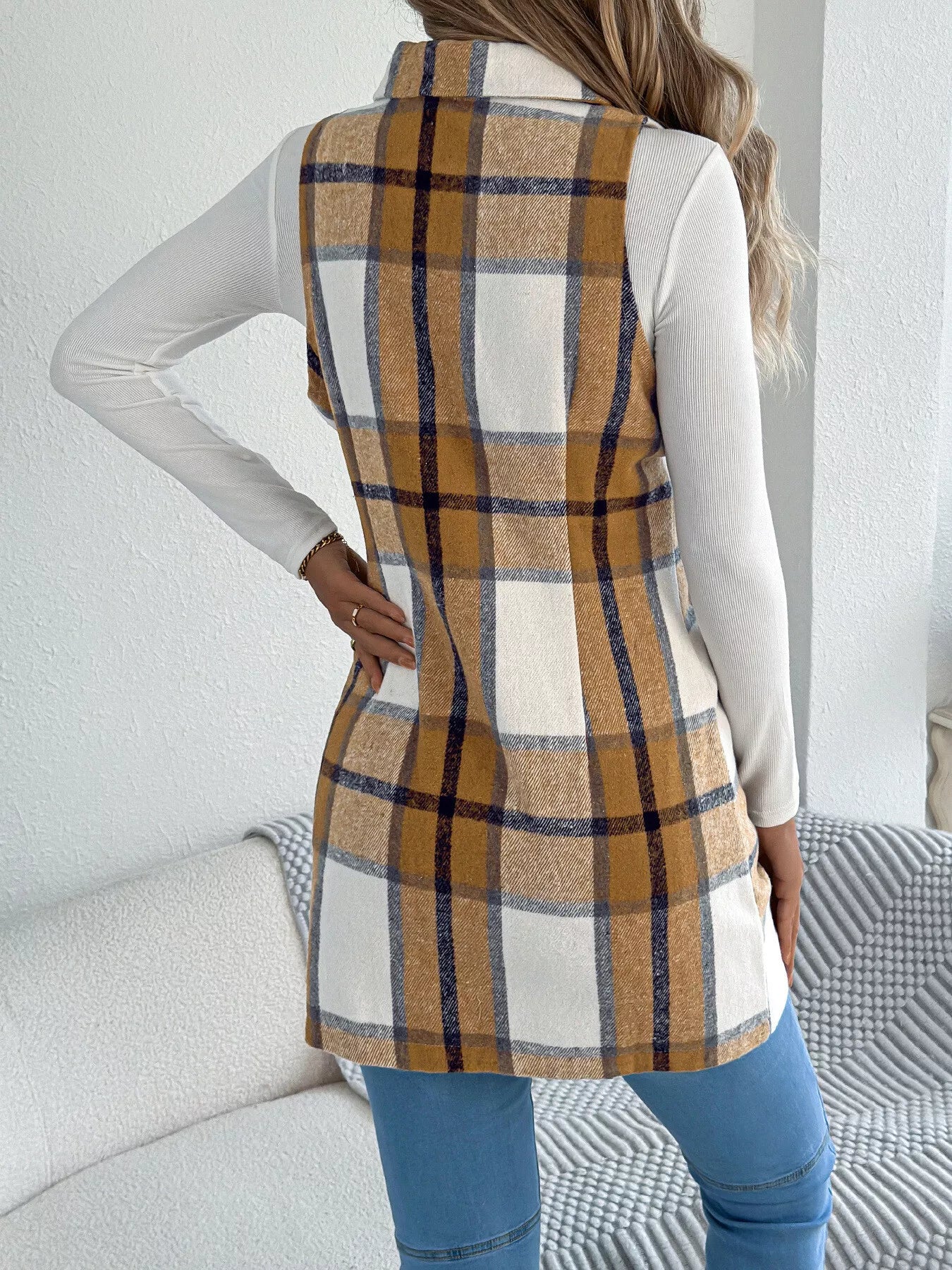 Women’s khaki plaid double-breasted long vest coat with pockets styled over a white turtleneck and jeans.