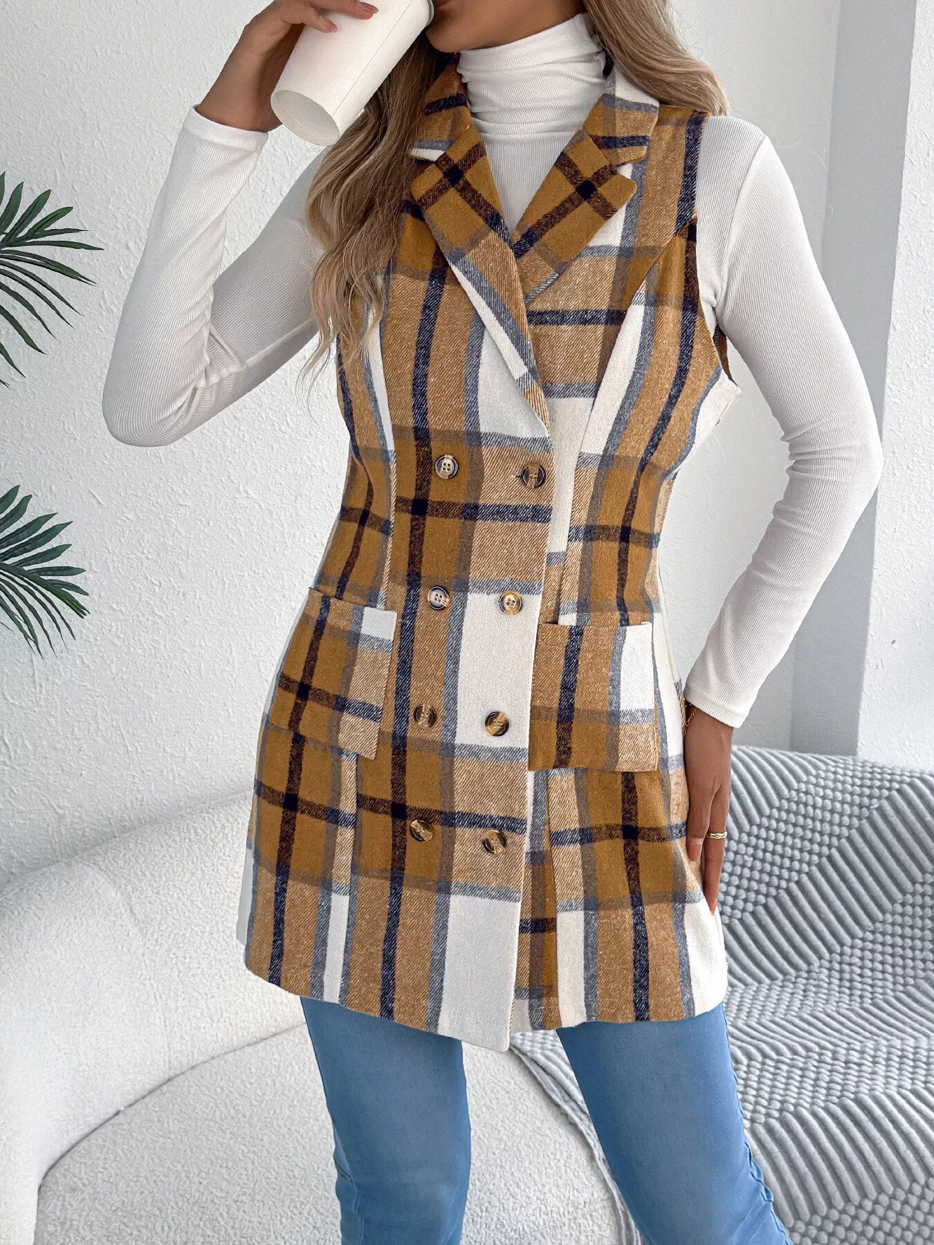 Women’s khaki plaid double-breasted long vest coat with pockets styled over a white turtleneck and jeans.