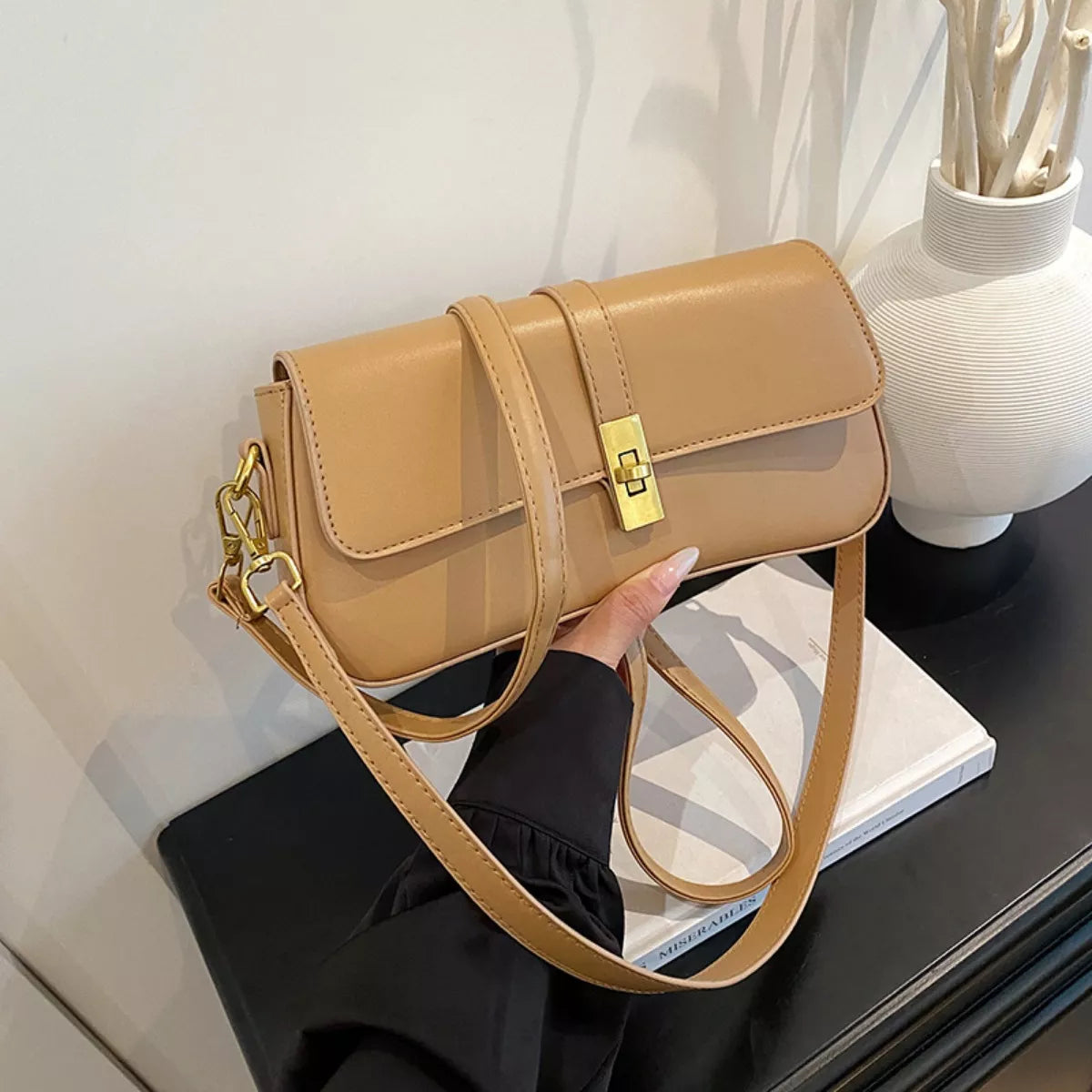 Khaki rectangular crossbody handbag with a gold turn-lock buckle and adjustable shoulder strap displayed on a modern tabletop.