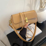 Khaki rectangular crossbody handbag with a gold turn-lock buckle and adjustable shoulder strap displayed on a modern tabletop.