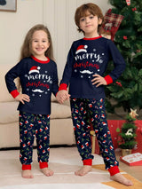 Boy and girl wearing matching navy Merry Christmas pajama sets with red cuffs and holiday-print pants beside a decorated Christmas tree.