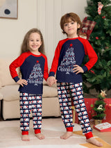 Kids wearing matching Christmas pajamas with navy tops, red raglan sleeves, festive Christmas tree lettering, and coordinating printed pants.