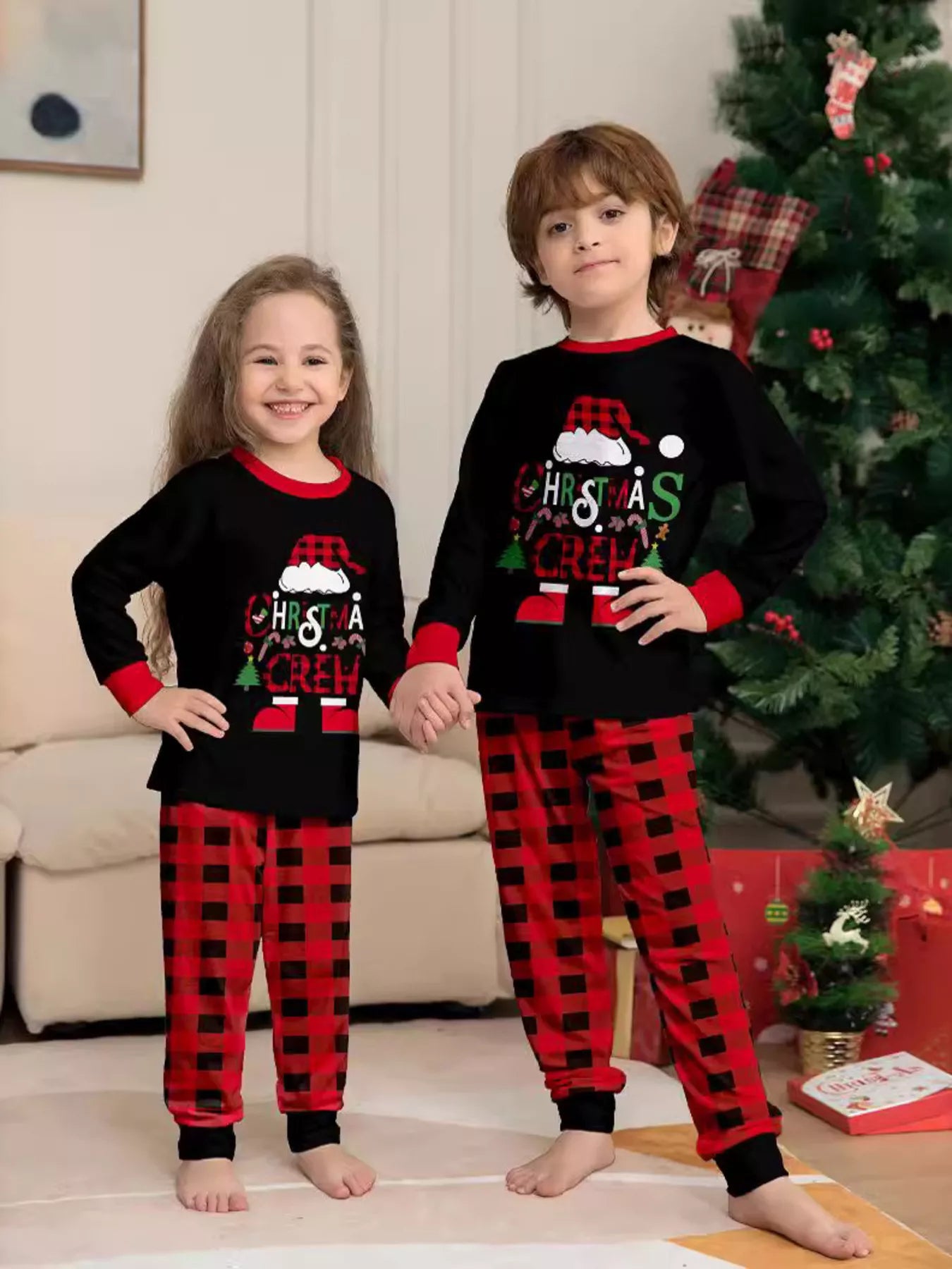 Boy and girl wearing matching Christmas Crew graphic pajama sets with black long-sleeve tops and red buffalo plaid pants.