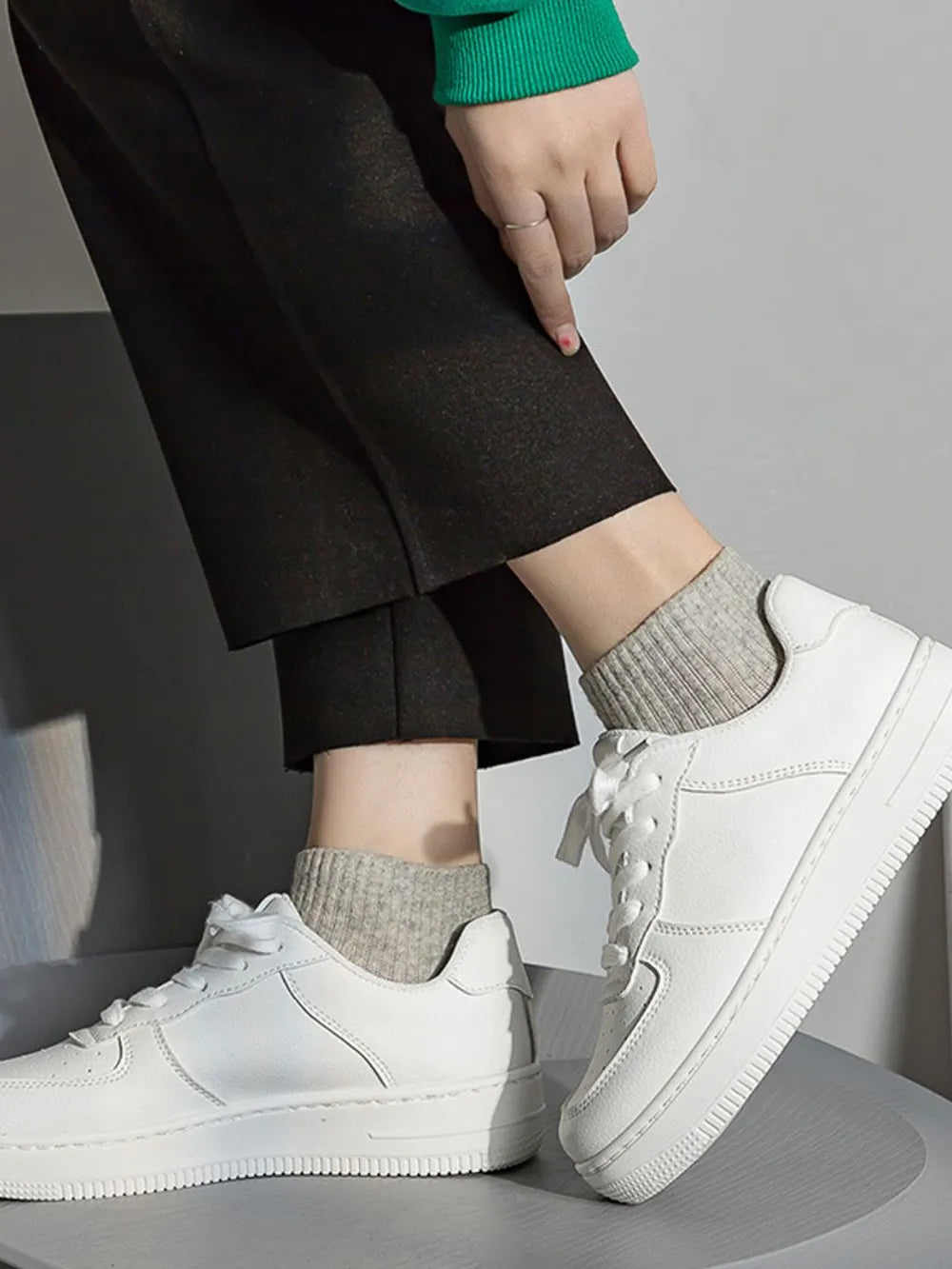 White sneakers worn with black pants and gray socks on a neutral background