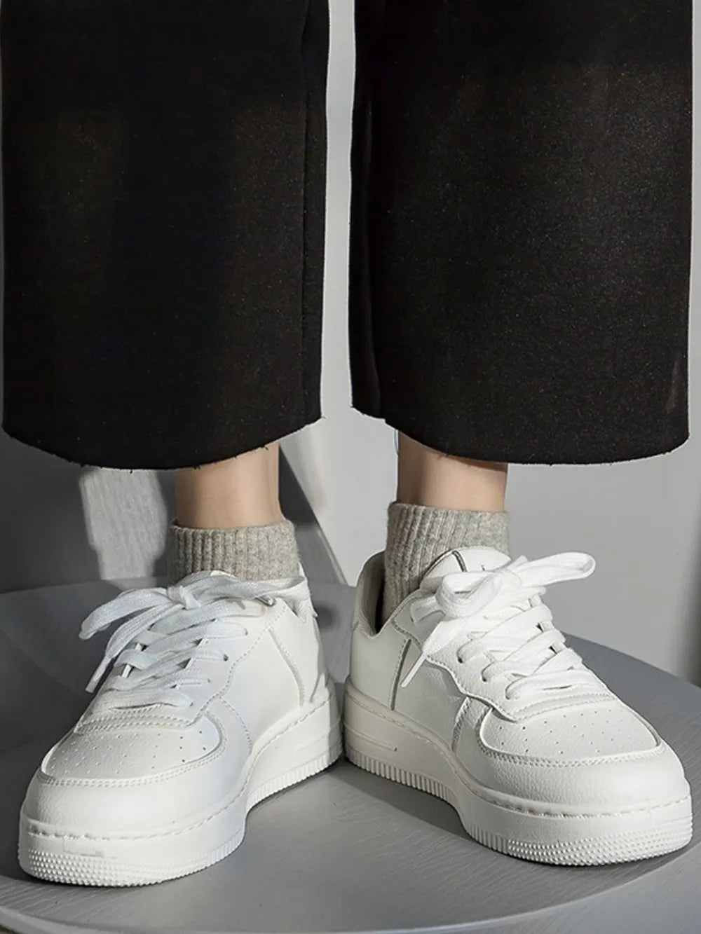 White sneakers worn with black pants and gray socks on a neutral background