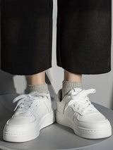 White sneakers worn with black pants and gray socks on a neutral background