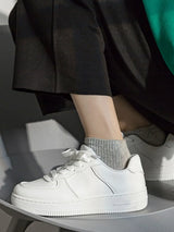 White sneakers worn with gray socks on a neutral background