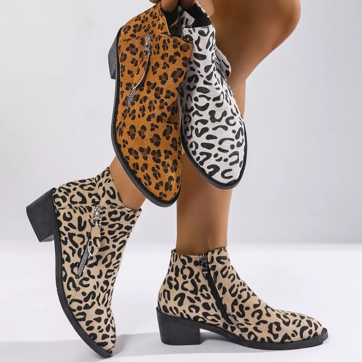 Woman wearing beige leopard-print ankle boots with block heels and side zipper details.