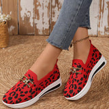 Red leopard print shoes with gold accents worn by a person on a textured floor.