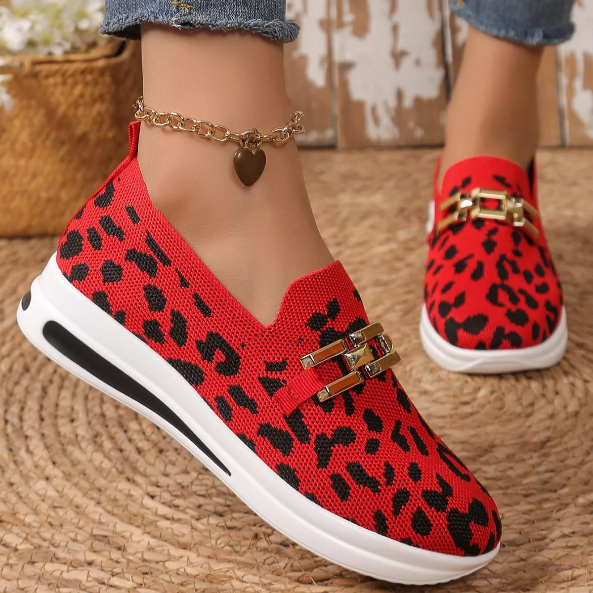Red leopard print shoes with gold accents worn by a person on a woven surface.