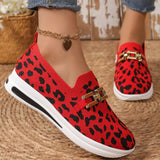 Red leopard print shoes with gold accents worn by a person on a woven surface.