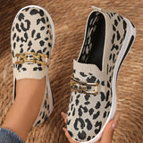 Leopard print slip-on shoes with gold accents held by a person on a woven surface.