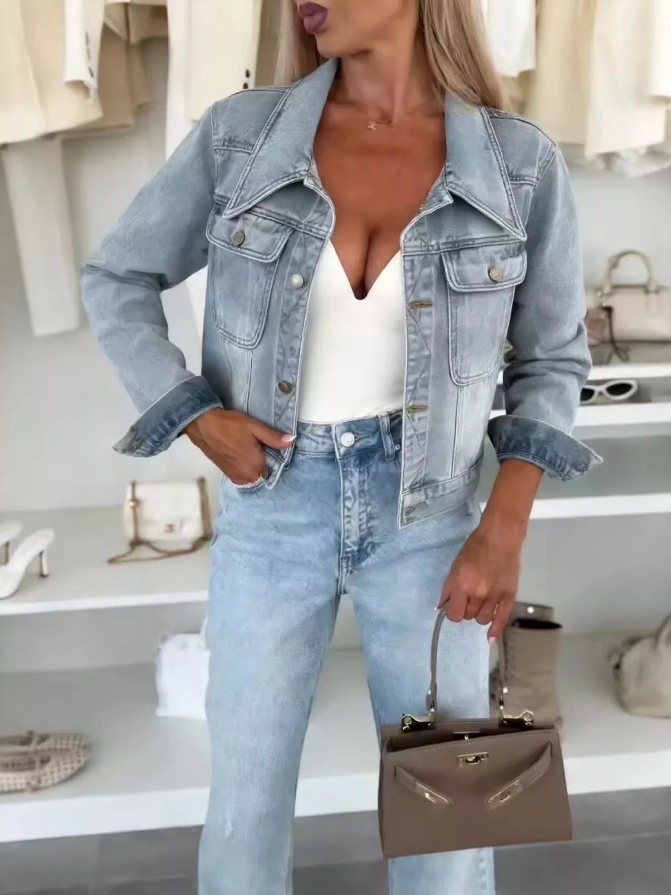 Woman wearing a light blue cropped denim jacket over a white top with light-wash jeans and a structured handbag, styled for a chic fall outfit.