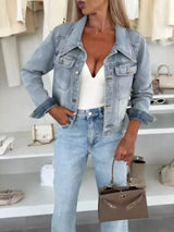 Woman wearing a light blue cropped denim jacket over a white top with light-wash jeans and a structured handbag, styled for a chic fall outfit.
