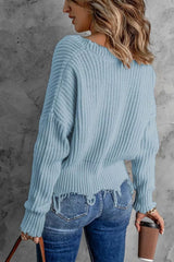 Woman wearing a light blue ribbed V-neck sweater with distressed raw hem and blue jeans.