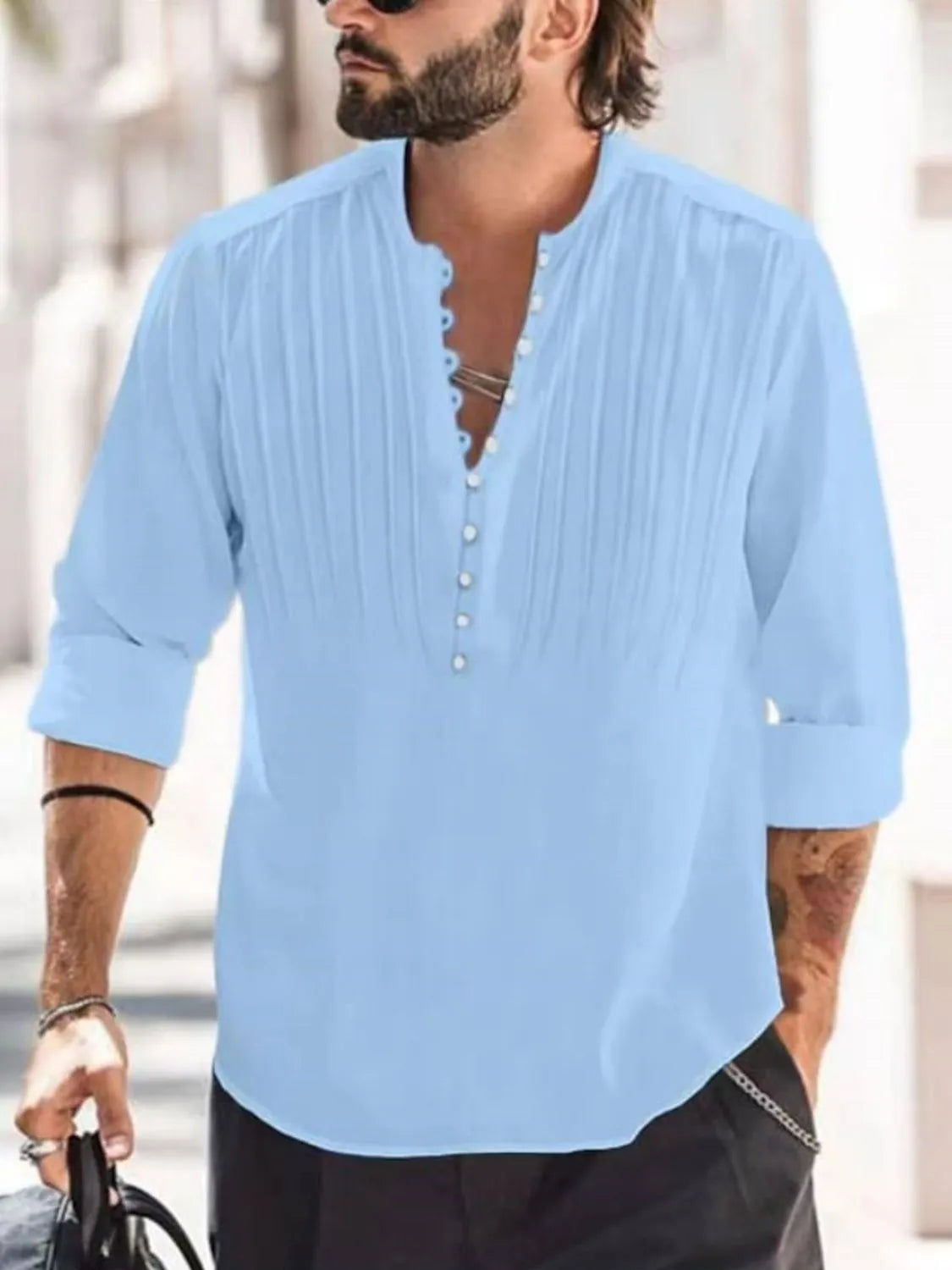 Man wearing a light blue button-detail long sleeve cotton polo with rolled sleeves and black pants.