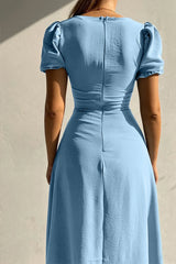 Woman wearing a light blue sweetheart-neck midi dress with puff sleeves, ruched detailing, and a button-front slit.