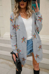 Woman wearing a light gray open-front cardigan with colorful star print, front pockets, denim shorts and black Western boots.