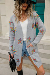 Woman wearing a light gray open-front cardigan with colorful star print, front pockets, denim shorts and black Western boots.