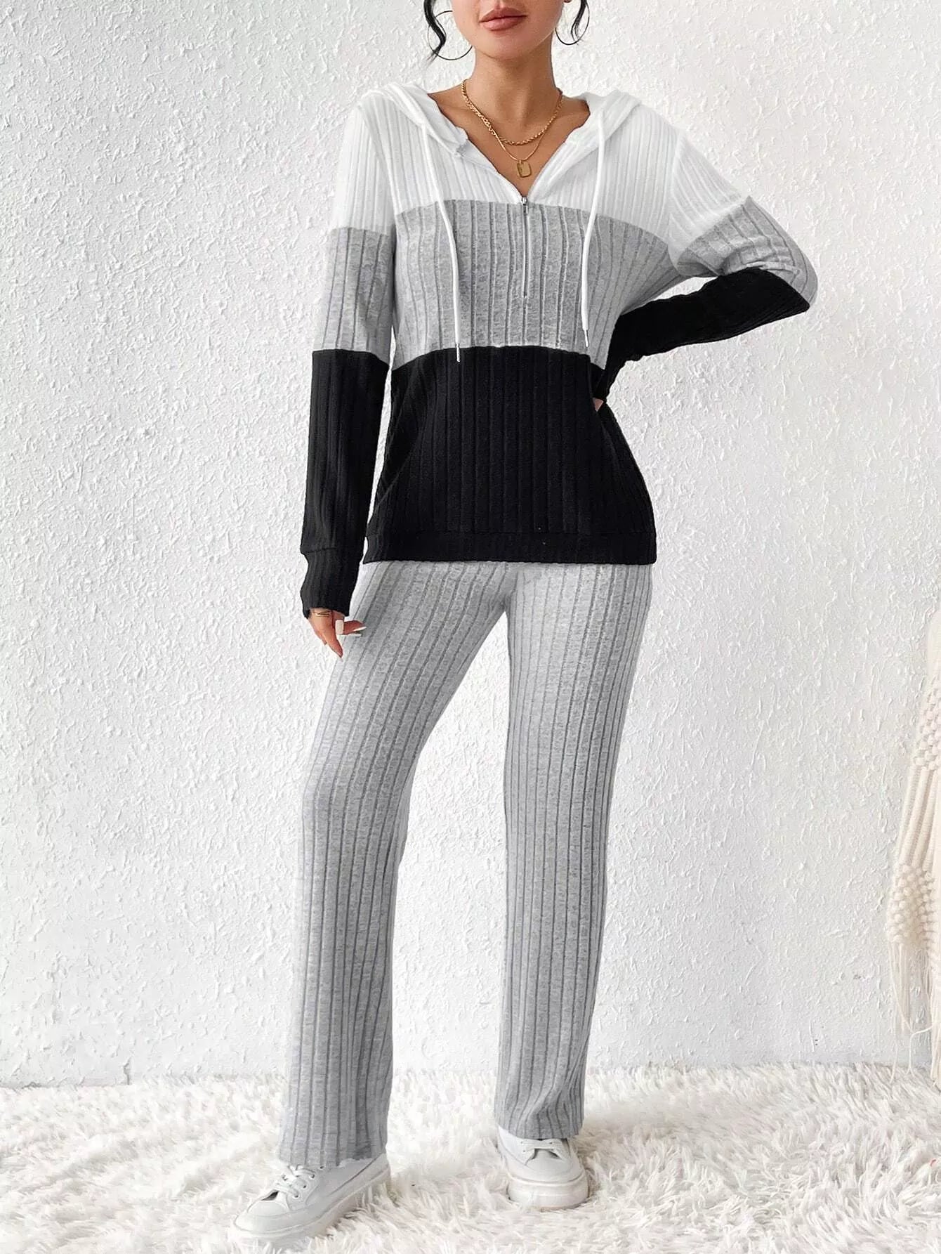Woman wearing a light gray, black and white color block half zip hooded top with matching ribbed-look pants.