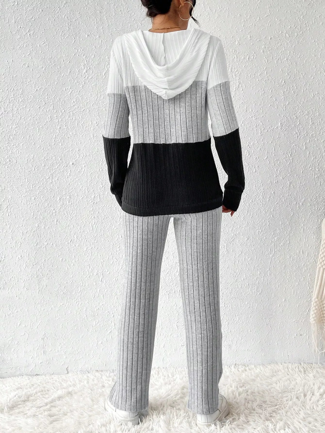 Woman wearing a light gray, black and white color block half zip hooded top with matching ribbed-look pants.