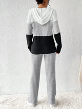 Woman wearing a light gray, black and white color block half zip hooded top with matching ribbed-look pants.