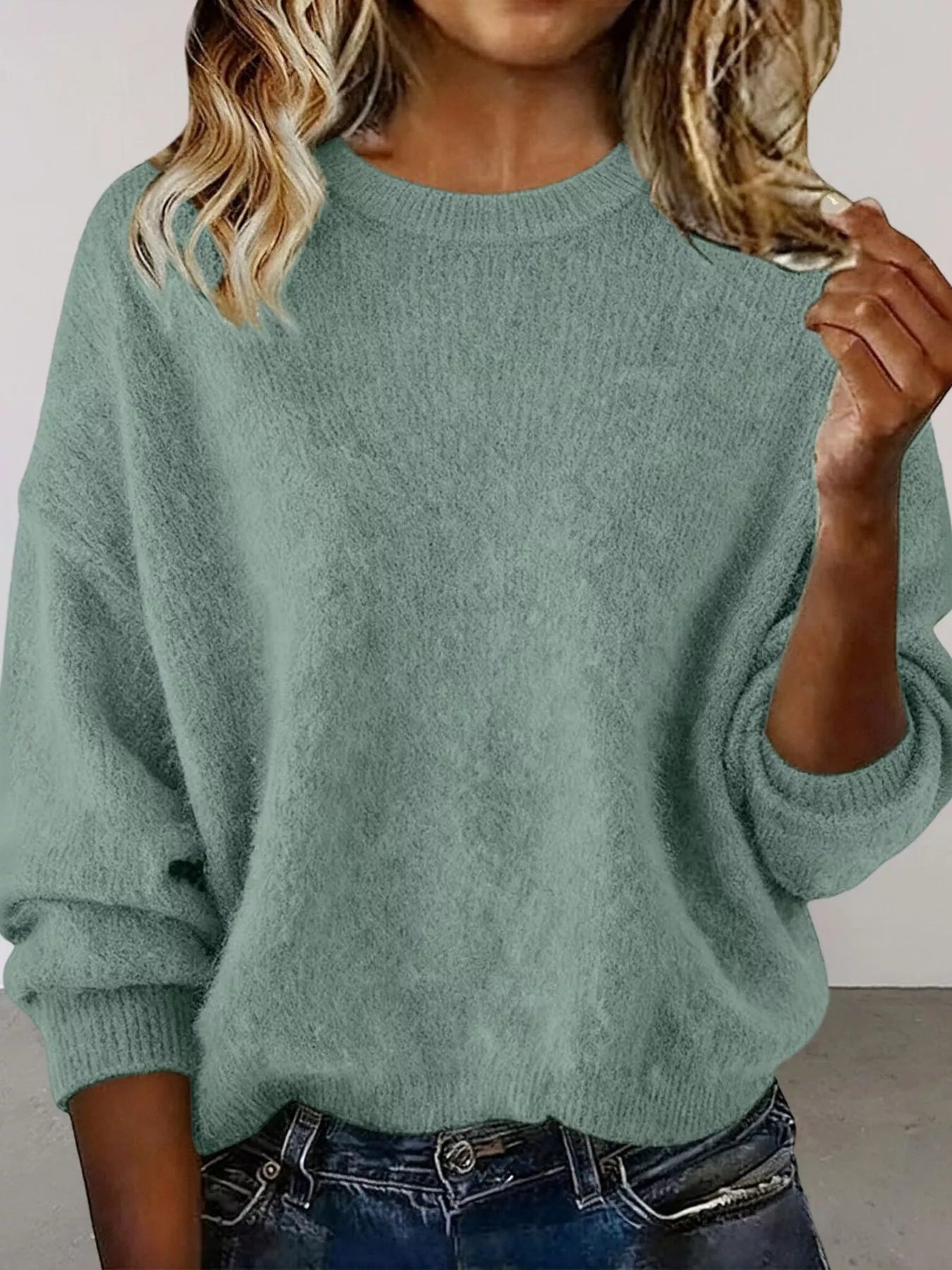 Woman wearing a light green round neck dropped shoulder sweater with dark-wash jeans.
