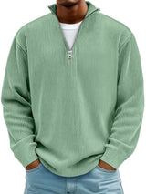 Man wearing a light green ribbed corduroy quarter zip pullover sweatshirt layered over a white shirt.