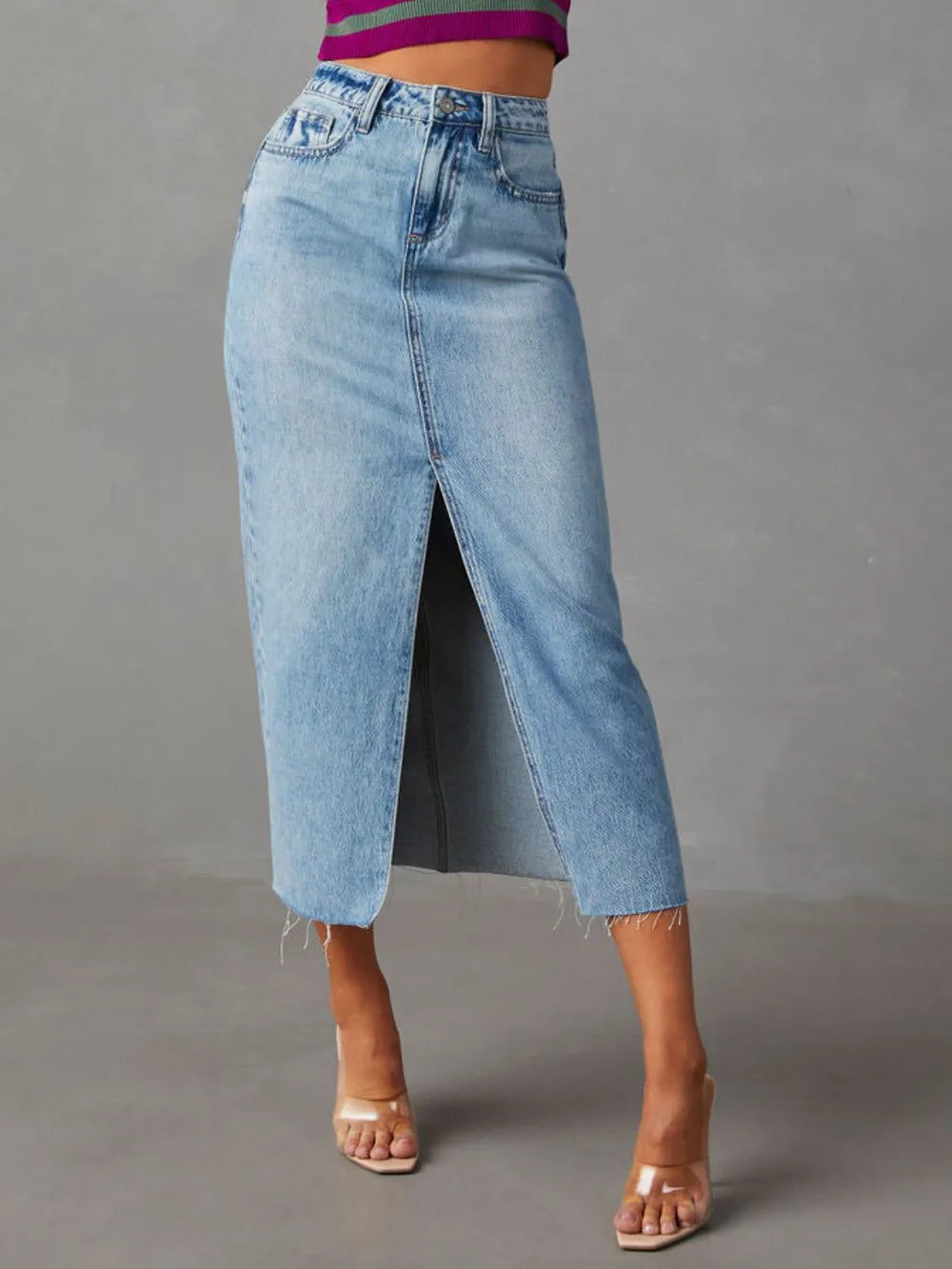 Woman wearing a light wash denim midi skirt with front slit, pockets and raw hem.