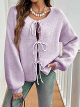 Woman wearing a light purple tie-front long sleeve knit cardigan with three bow ties paired with blue jeans.