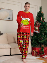 Man modeling matching red Grinch-themed Christmas pajamas with festive graphic tops and red and black character-print pants.