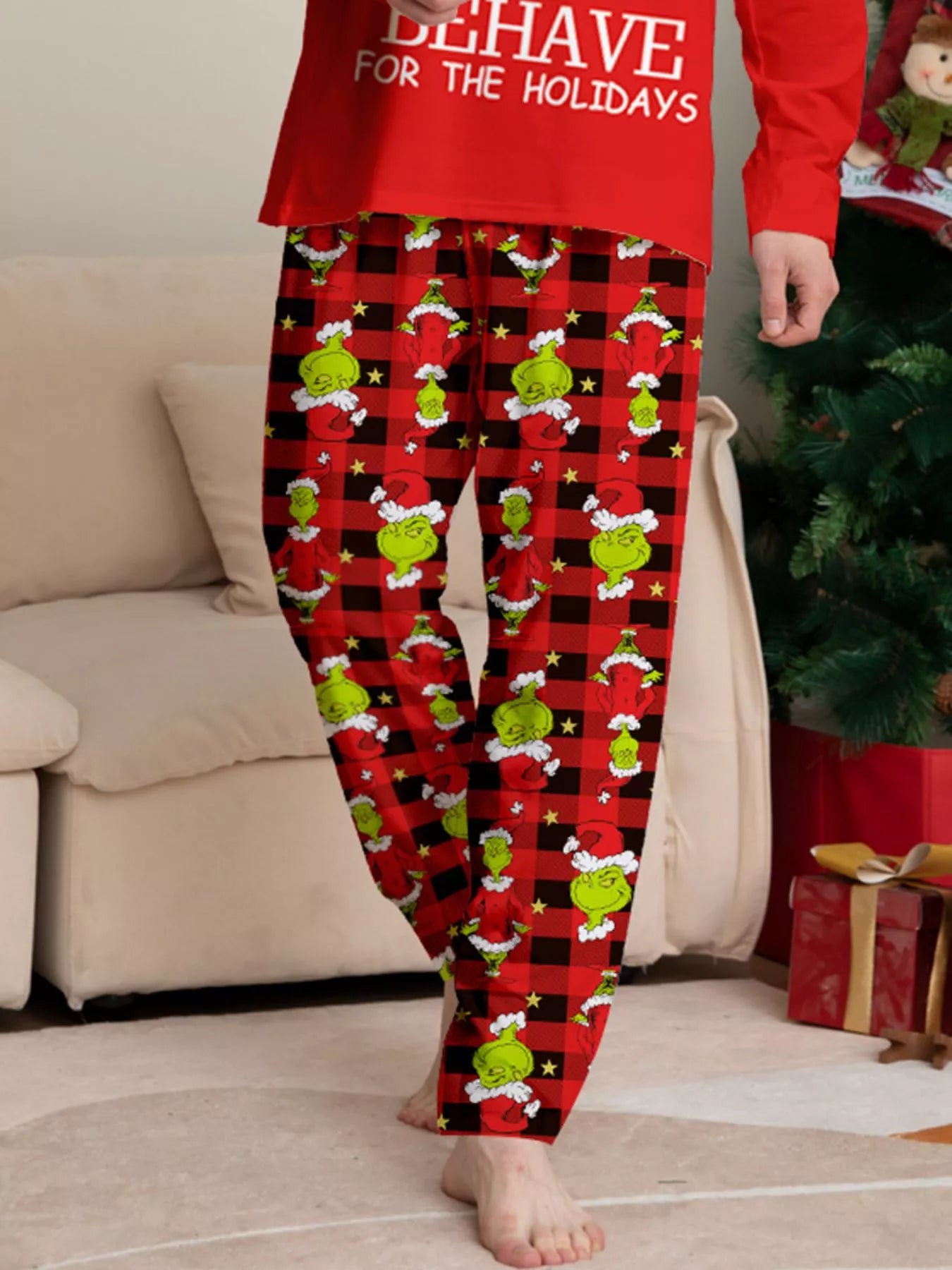 Man modeling matching red Grinch-themed Christmas pajamas with festive graphic tops and red and black character-print pants.
