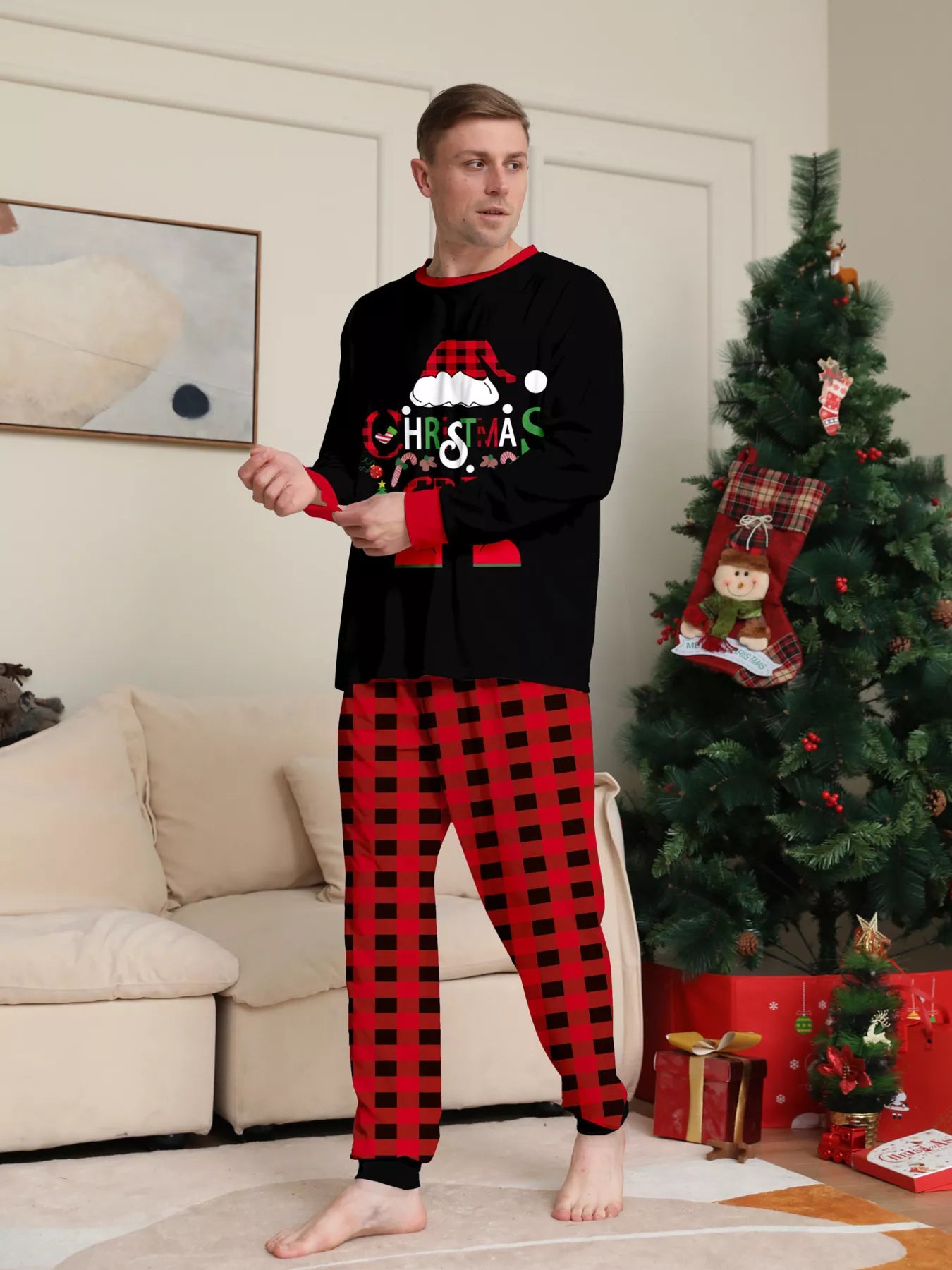 Dad modeling matching Christmas Crew pajama sets with festive black graphic tops and red and black plaid pants.