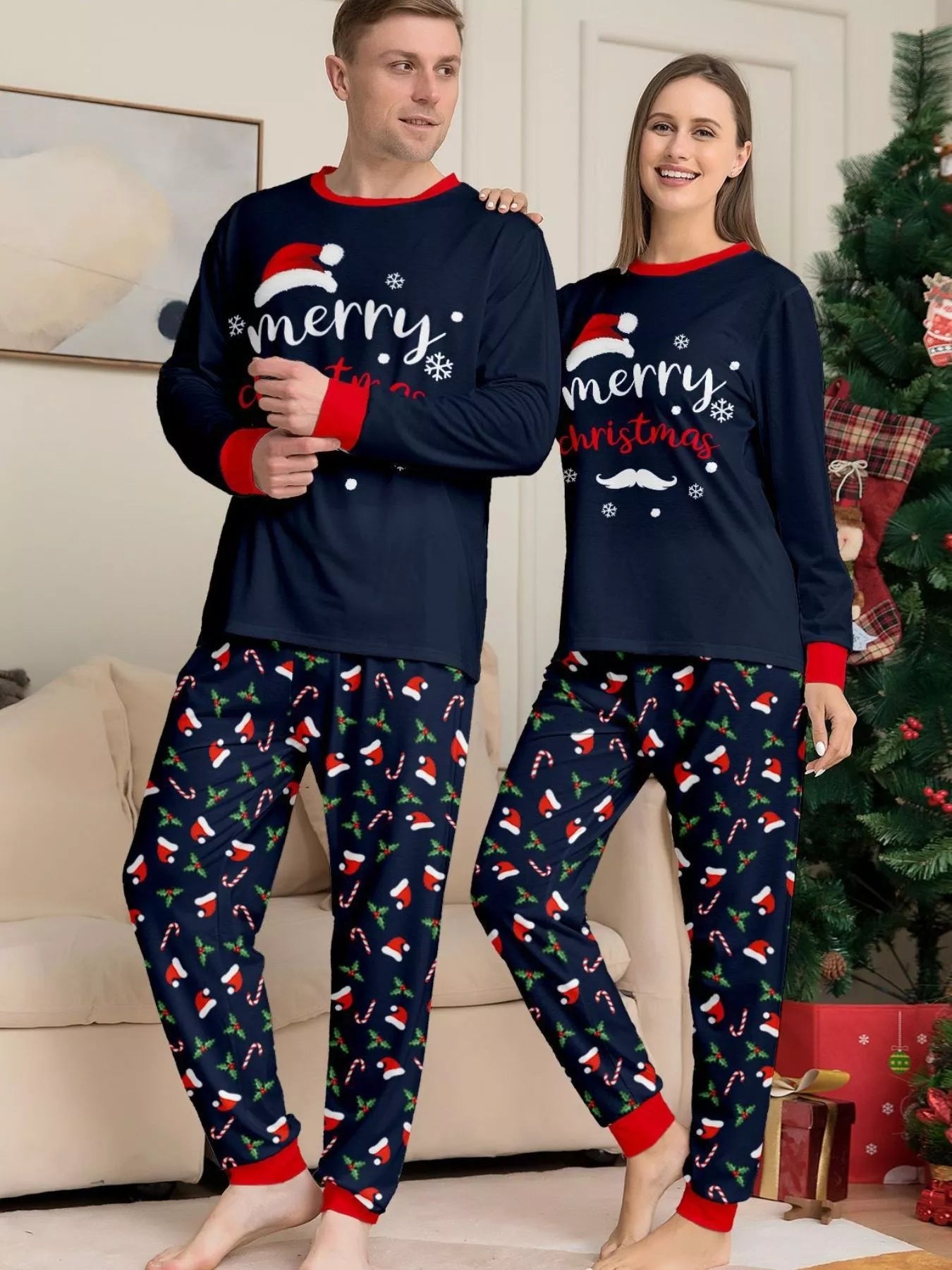 Man and woman wearing coordinating navy blue Merry Christmas pajama sets with red trim and holiday-print pants.