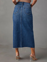 Woman wearing a medium wash denim midi skirt with front slit, pockets and raw hem.