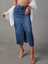 Woman wearing a medium wash denim midi skirt with front slit, pockets and raw hem.