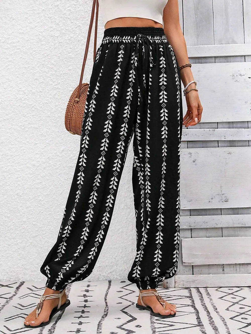 Person wearing black patterned pants with a white background front view.