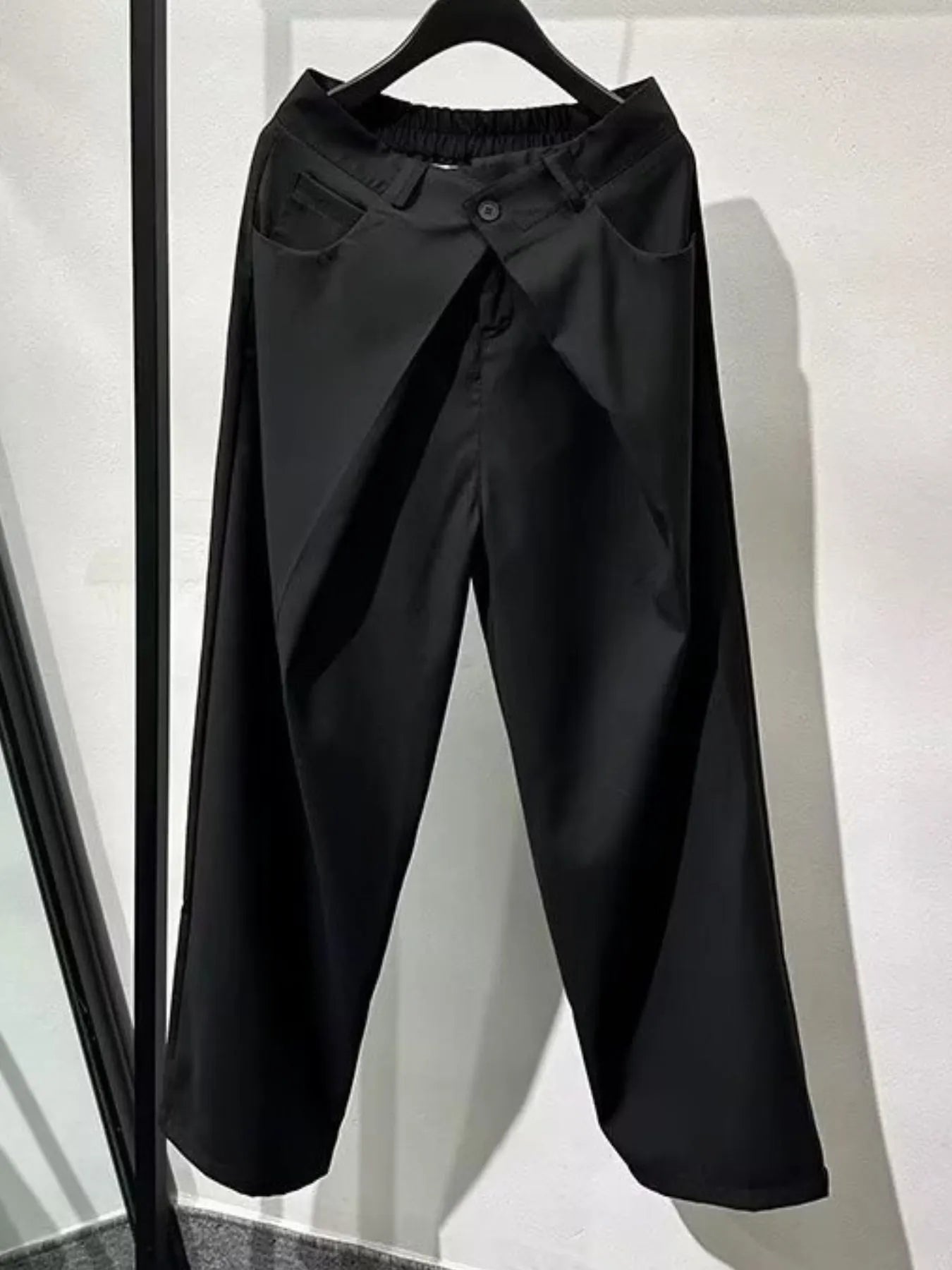 Men's black wide leg pleated pants with a button-front waistband and relaxed, full-length silhouette, styled with a black top and chunky black shoes.
