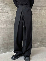 Men's black wide leg pleated pants with a button-front waistband and relaxed, full-length silhouette, styled with a black top and chunky black shoes.