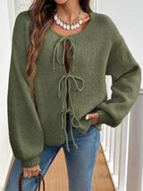 Woman wearing a military green tie-front long sleeve knit cardigan with three bow ties paired with blue jeans.