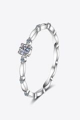 Rhodium-plated 925 sterling silver minimalist ring featuring a 0.1 carat round moissanite center stone with delicate sparkling accents on a teal background.