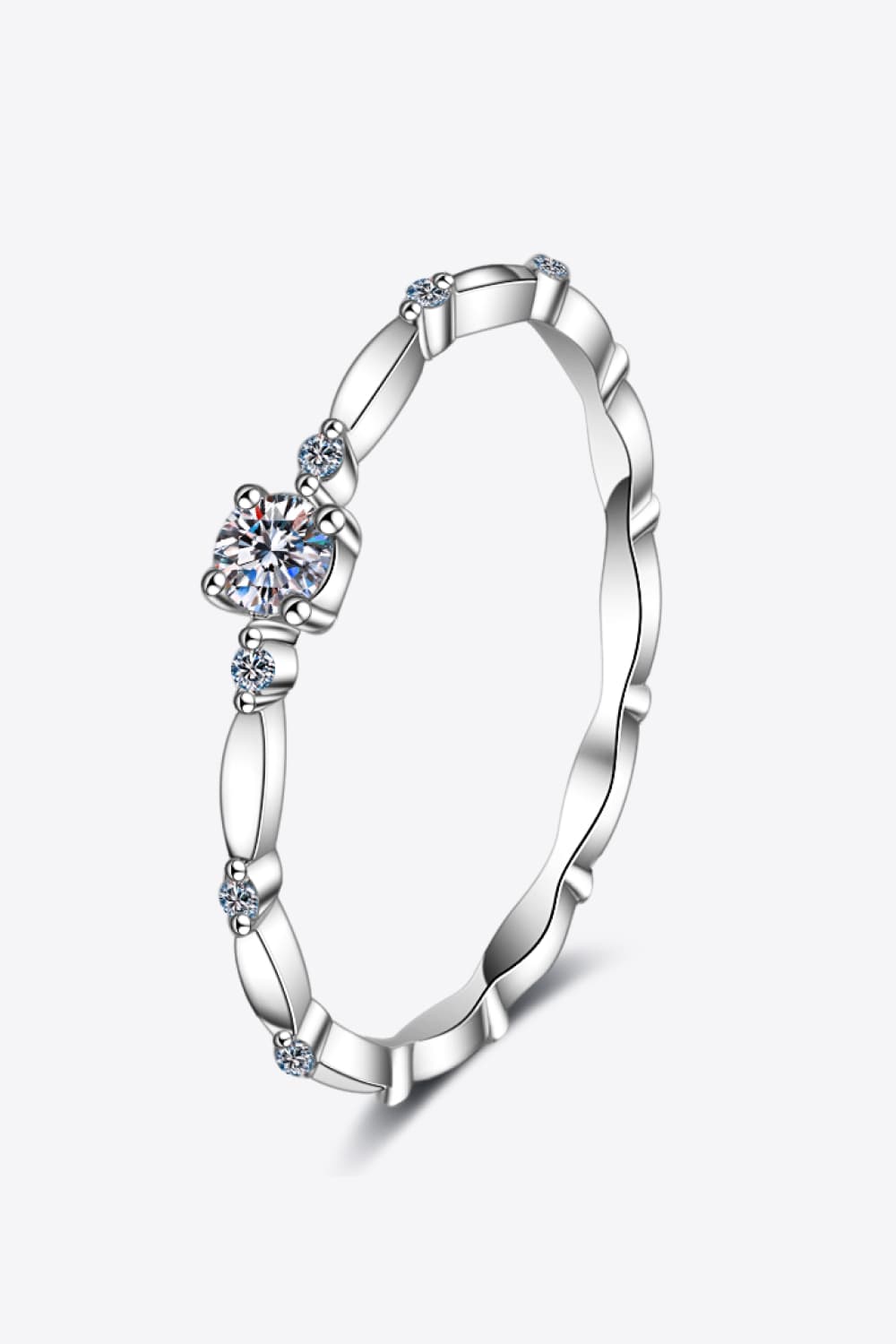 Rhodium-plated 925 sterling silver minimalist ring featuring a 0.1 carat round moissanite center stone with delicate sparkling accents on a teal background.