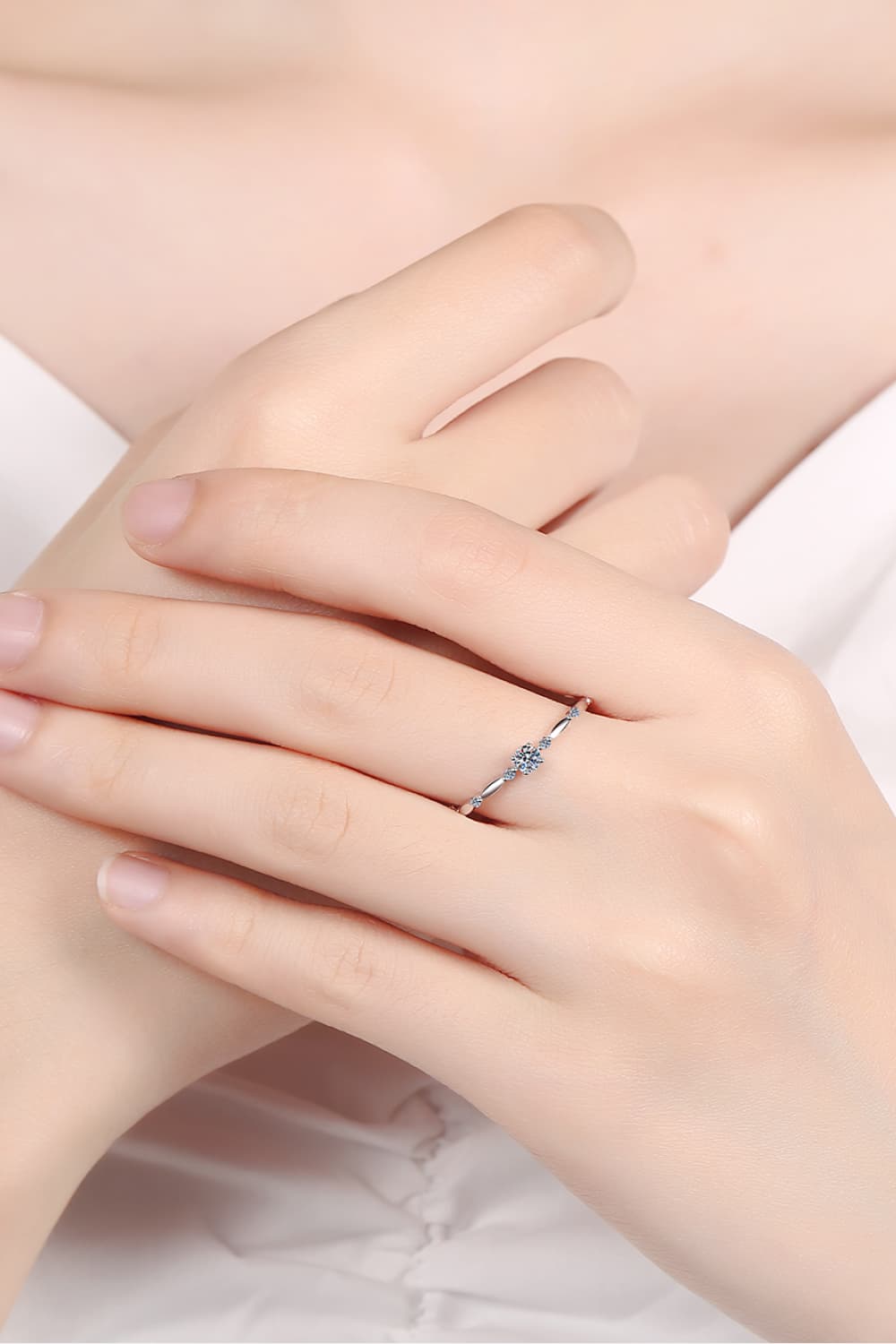 Rhodium-plated 925 sterling silver minimalist ring featuring a 0.1 carat round moissanite center stone with delicate sparkling accents on a teal background.