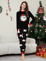 Mom wearing matching black Christmas pajamas with polar bear print, colorful holiday lights and red trim beside a Christmas tree.