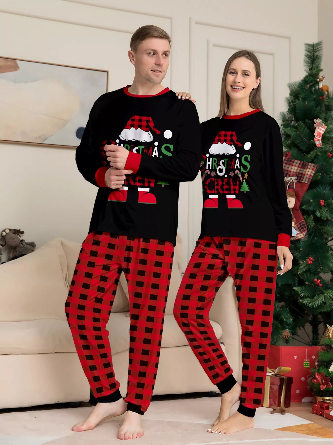 Mom and Dad modeling matching Christmas Crew pajama sets with festive black graphic tops and red and black plaid pants.