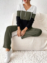 Woman wearing a moss, black and white color block half zip hooded top with matching ribbed-look pants.